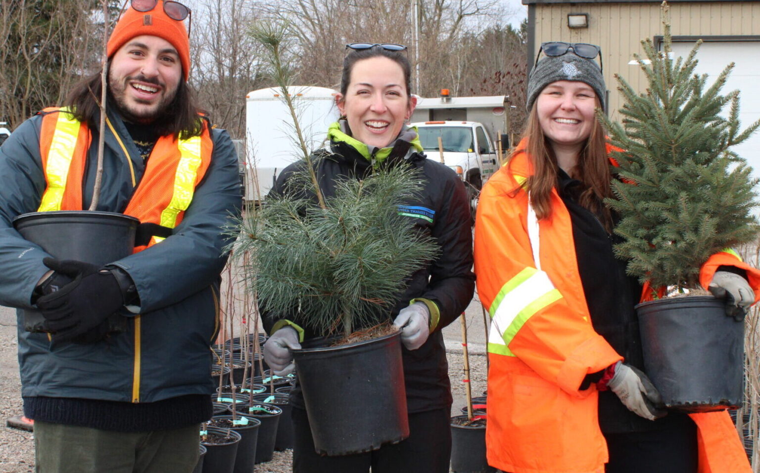 Three people holding potted tree seedlings